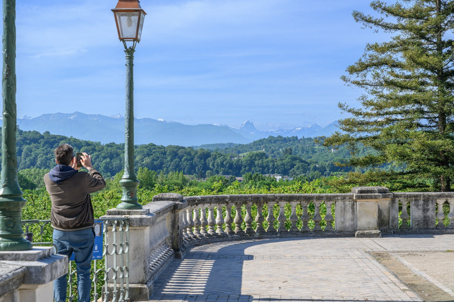 Boulevard des Pyrénées, a man takes a photo of the Pyrenees mountain range near the funicular